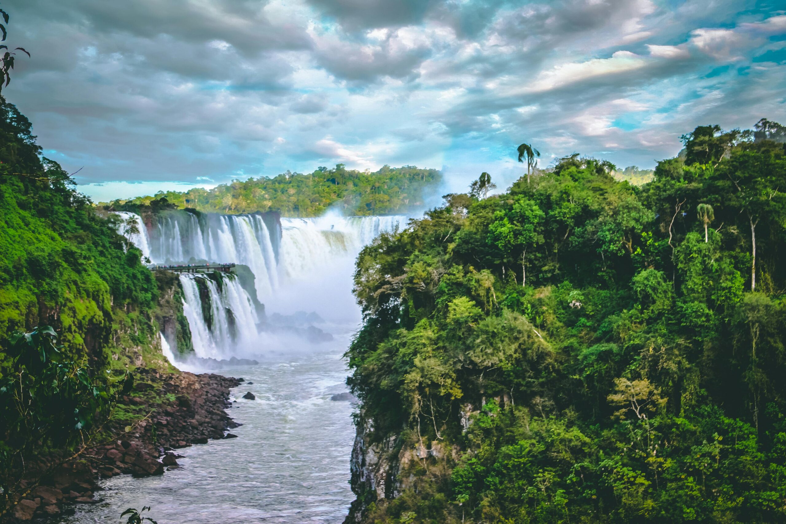 Breathtaking view of towering waterfalls surrounded by vibrant green jungle and dramatic clouds.